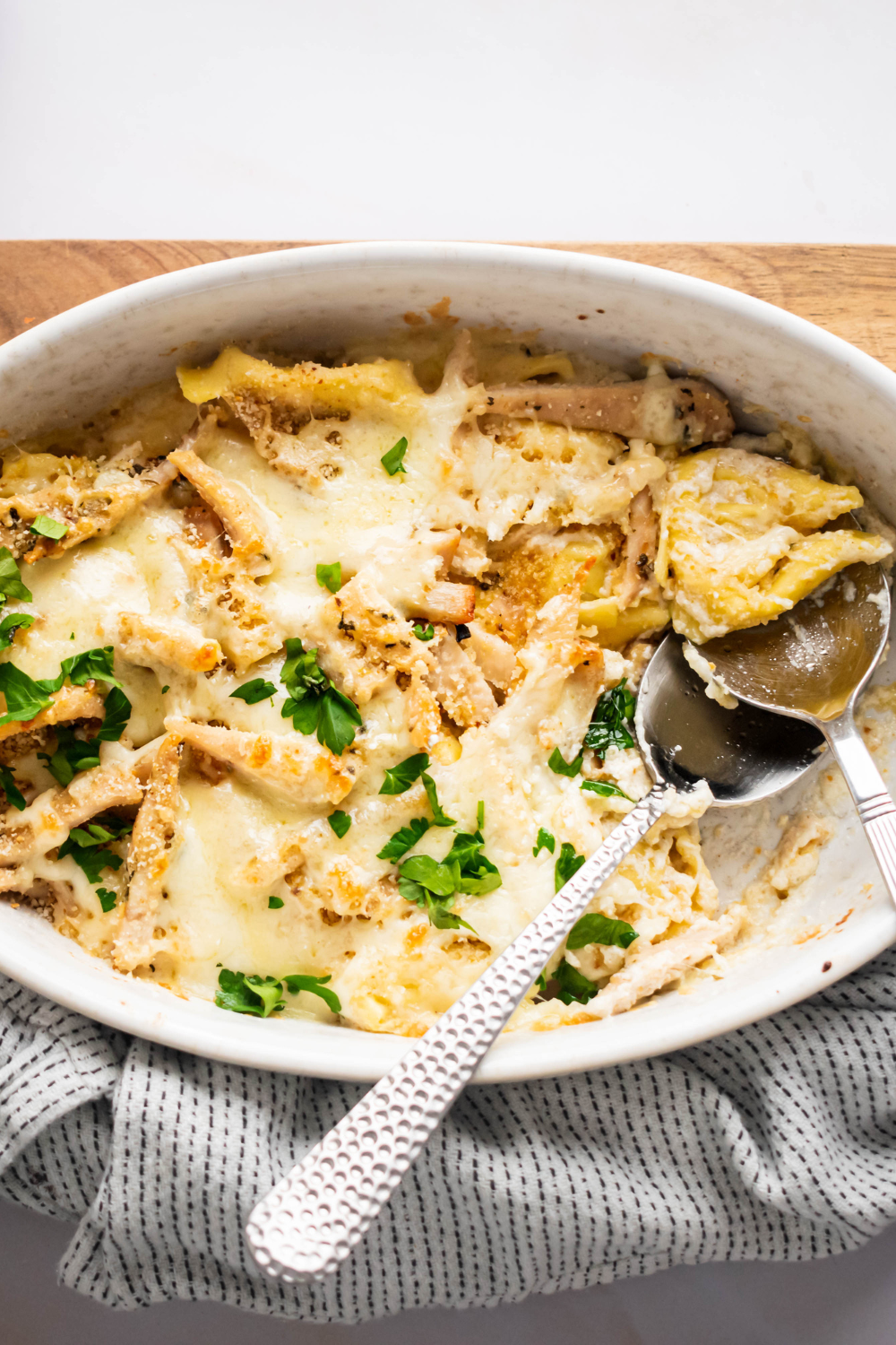 Teaspoons in a baking dish that is filled with asiago tortellini Alfredo with grilled chicken.