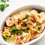 Breadcrumbs on top of giant cheese stuffed shells that have Alfredo sauce on them in a white casserole dish.