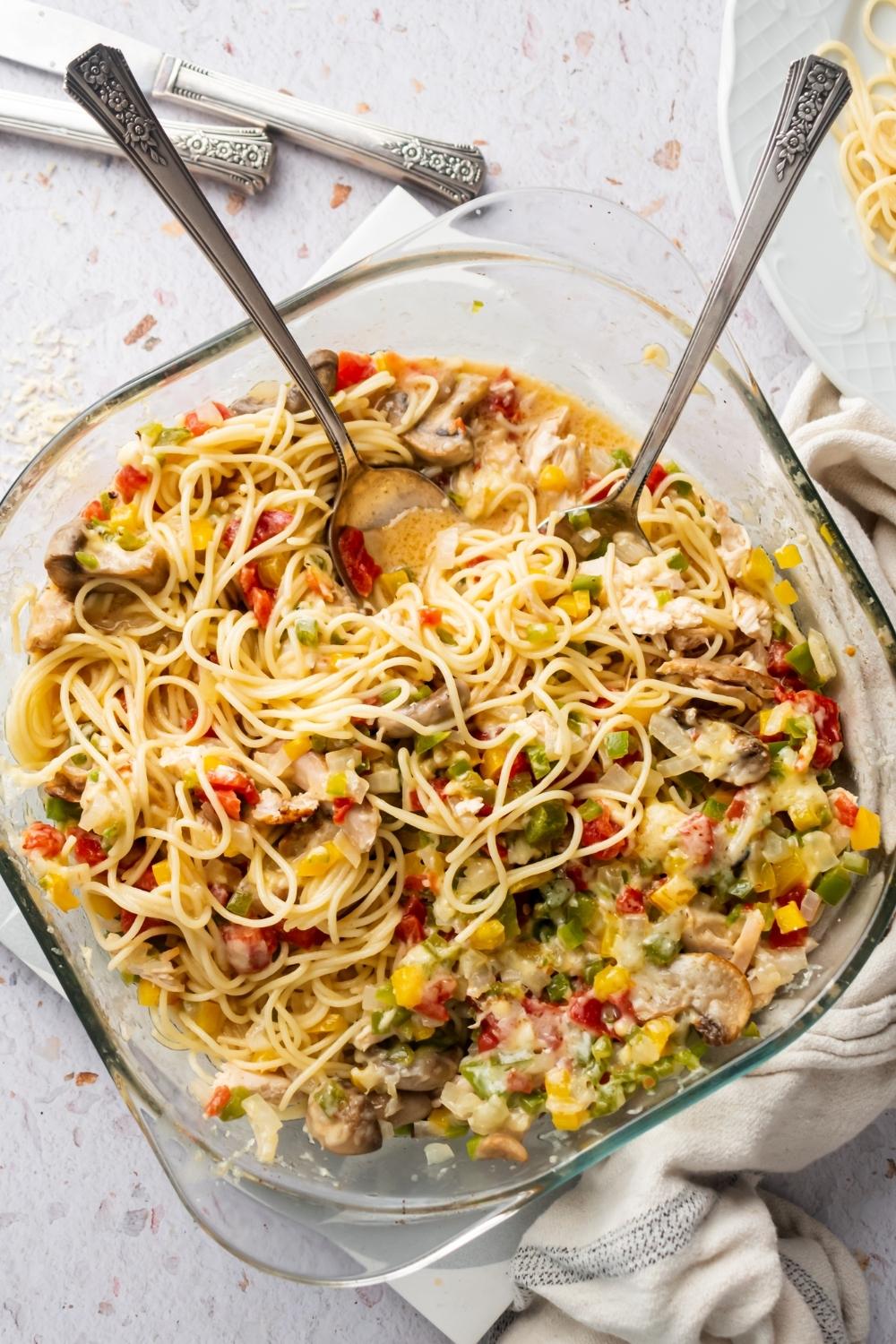 Spaghetti noodles and other chicken spaghetti ingredients in a glass casserole dish.