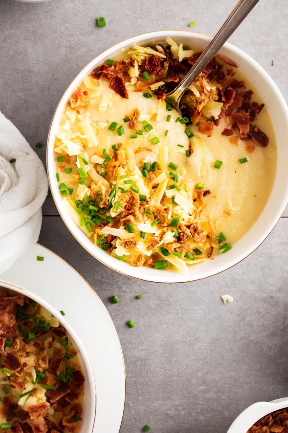 Crispy onions, green onions, bacon bits, and shredded cheese on top of potato soup in a white bowl.