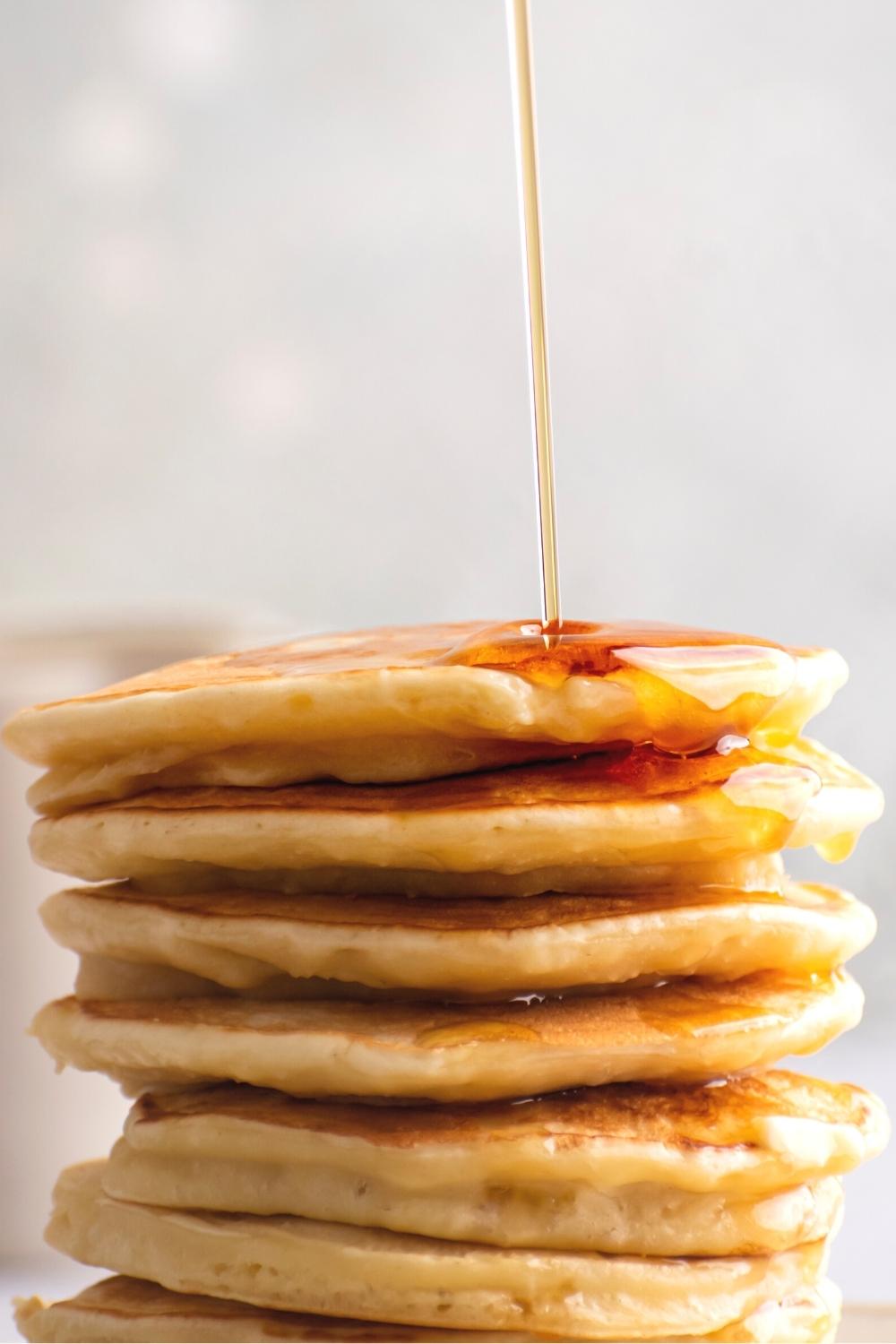 Maple syrup drizzling on top of a stack of six pancakes.