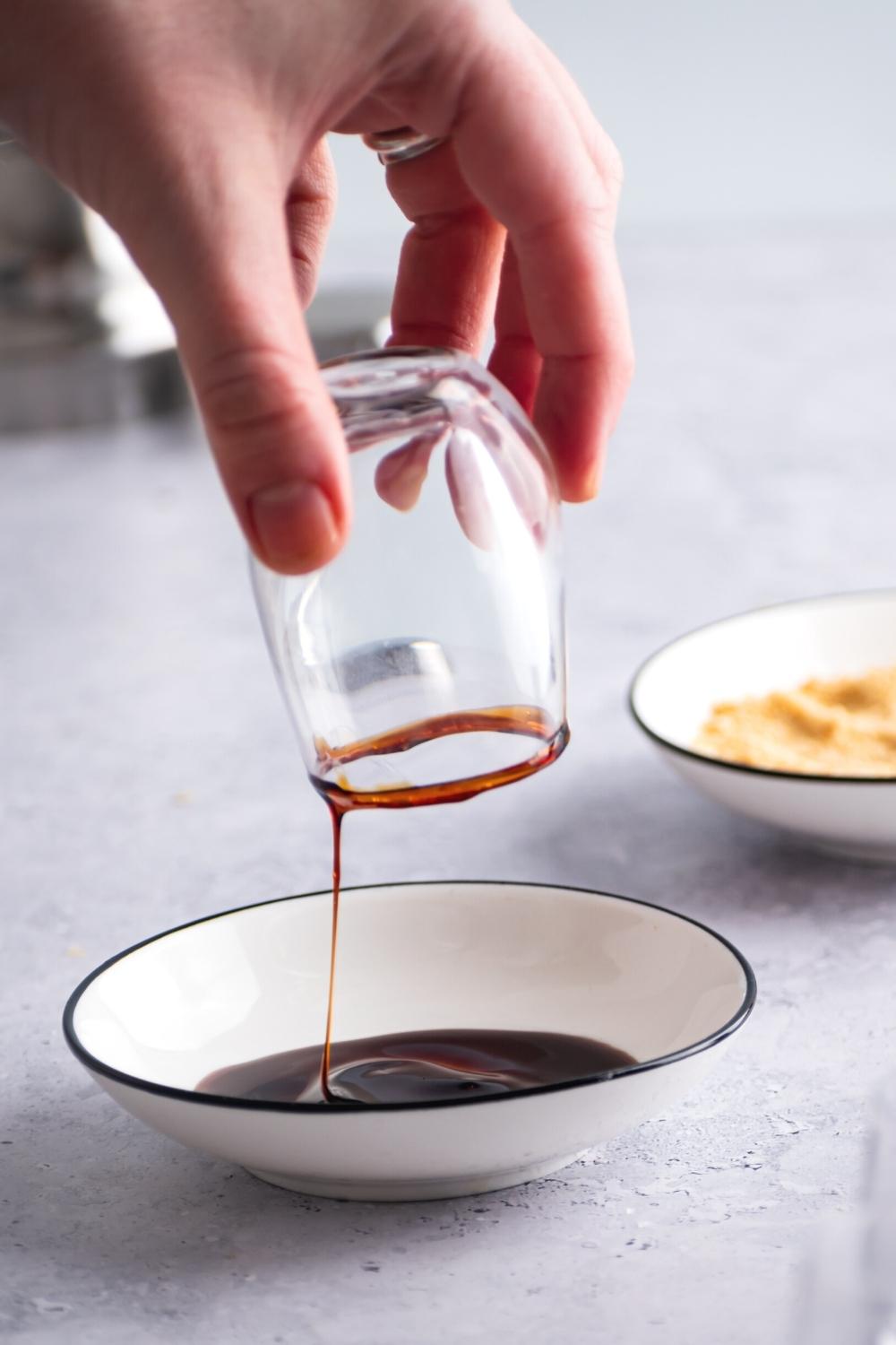A hand holding a shot glass upside down with caramel sauce on the rim dripping down into a bowl that is filled with the caramel sauce.
