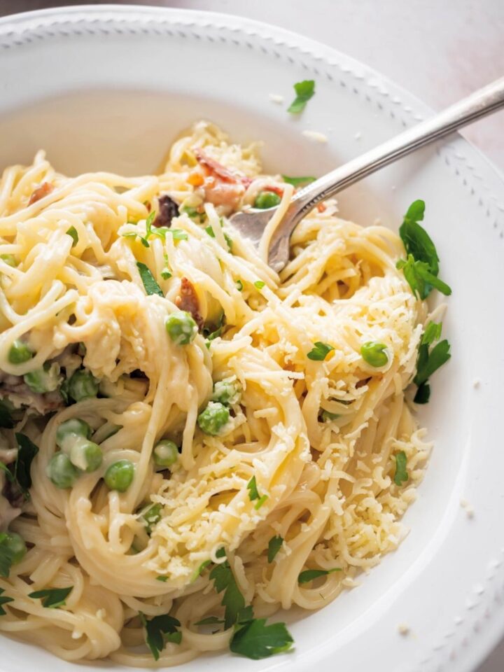 Part of a white ball that is filled with pasta carbonara. There's a fork submerged in the spaghetti.