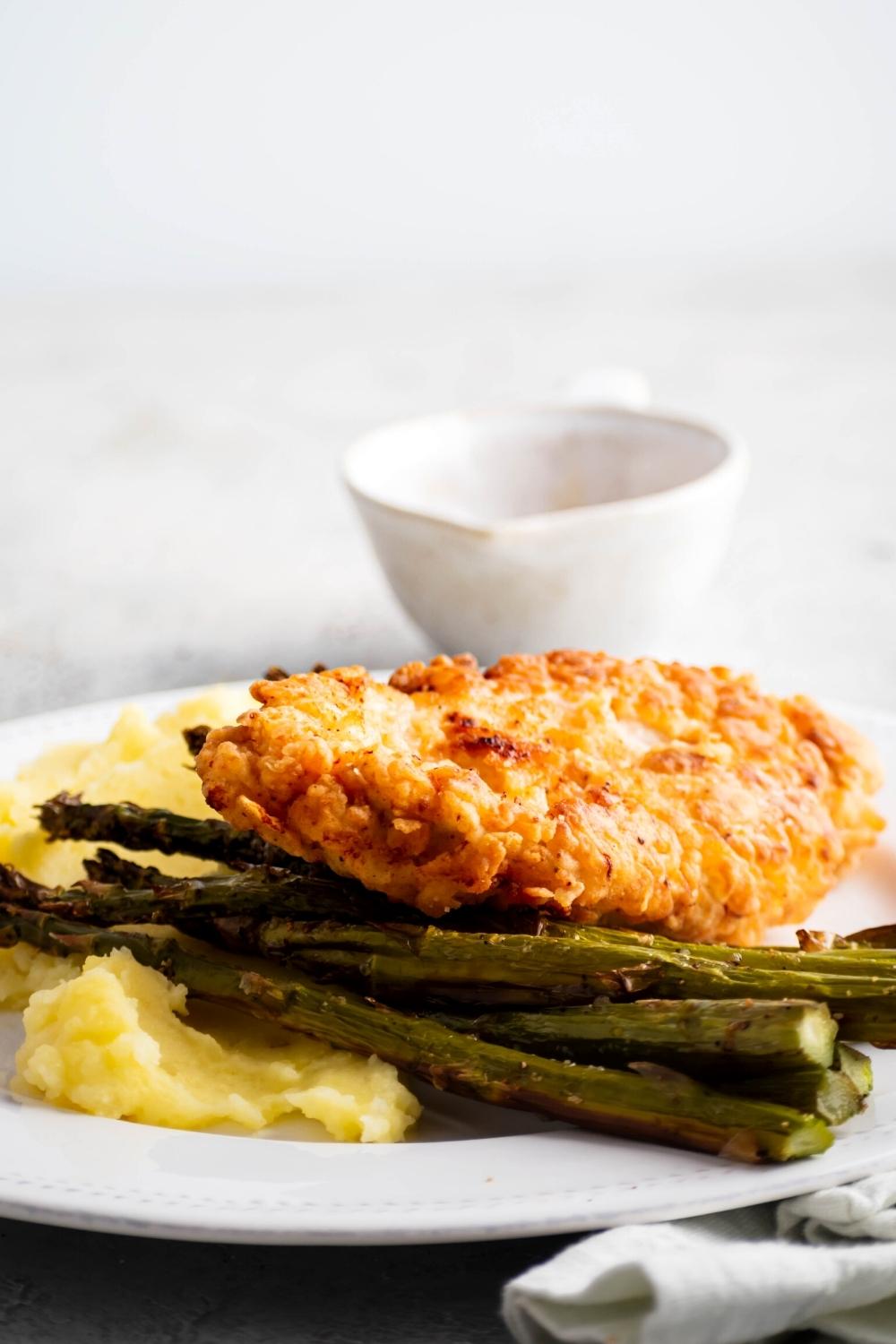 A piece of truffle honey chicken, asparagus spears, and mashed potatoes on a white plate.