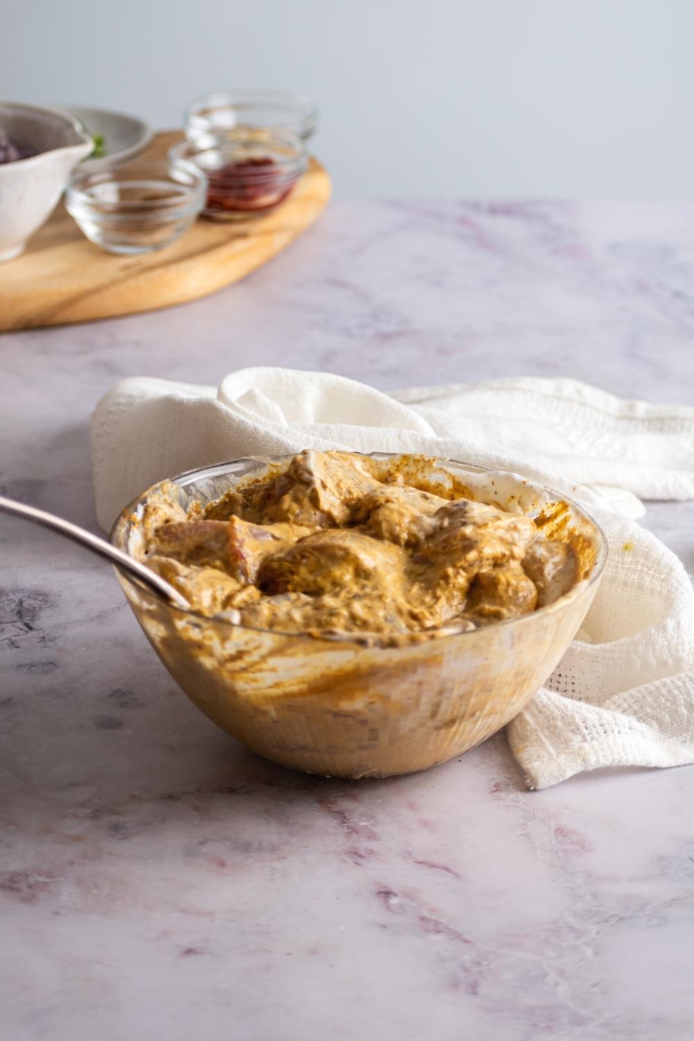 Chicken pieces mixed in a marinade for chicken 65 and a glass bowl.