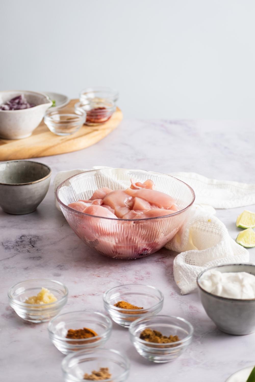 Bowl of raw chicken, and five bowls of Indian spices for chicken 65 in front of it.