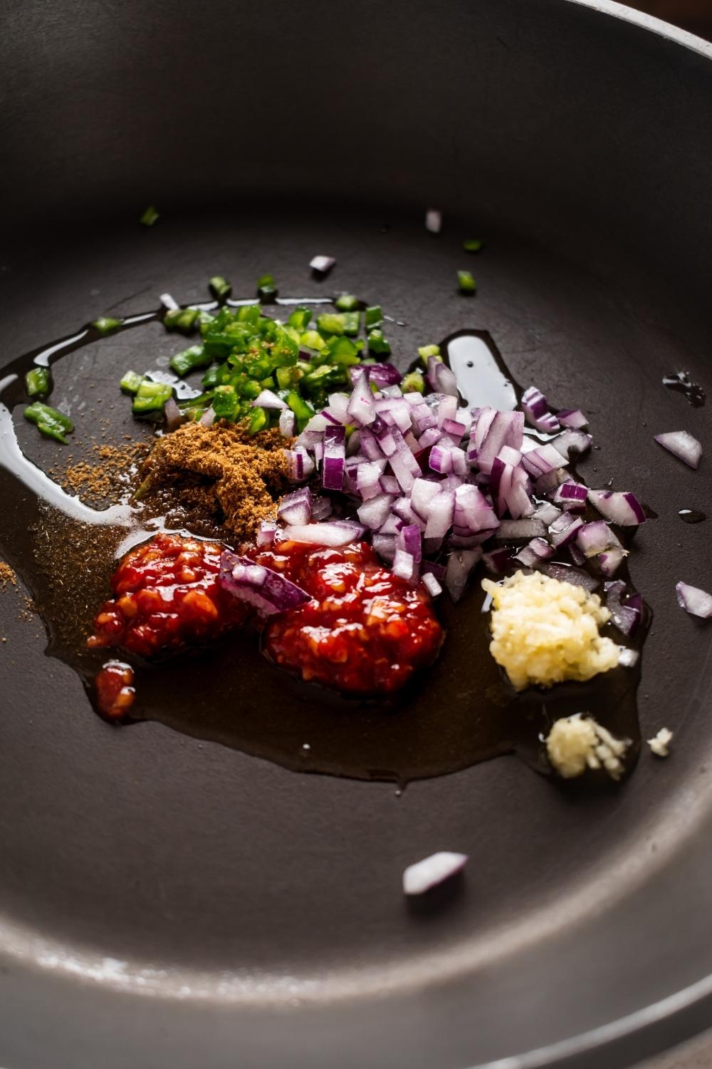 Red chili paste, garlic, curry powder, diced green onion, and diced red onion in a skillet.