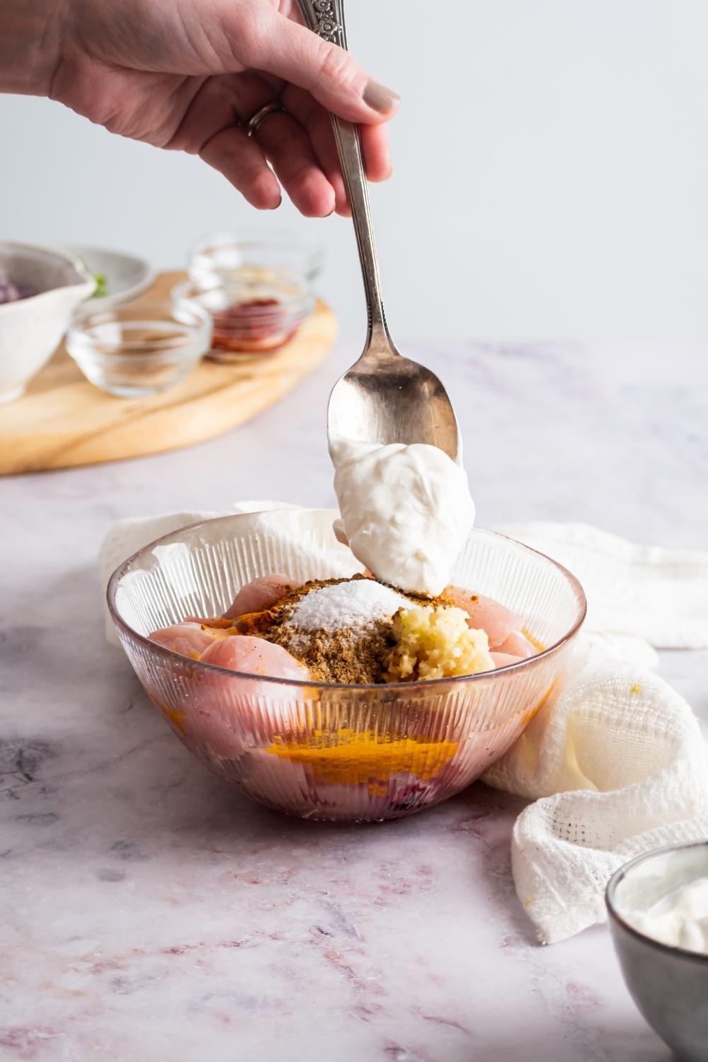 Hand holding a spoon full of cream over a bowl of chicken with Indian spices.