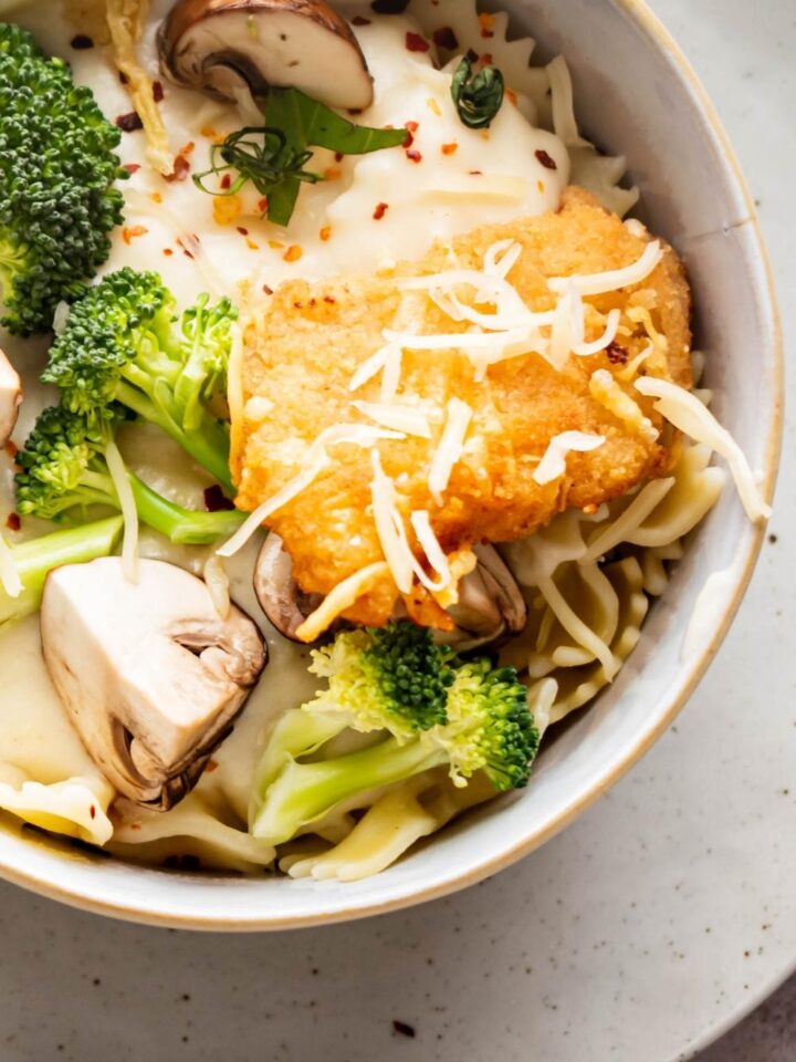 Part of a bowl with a piece of chicken fritta, some broccoli, and mushrooms with alfredo sauce.