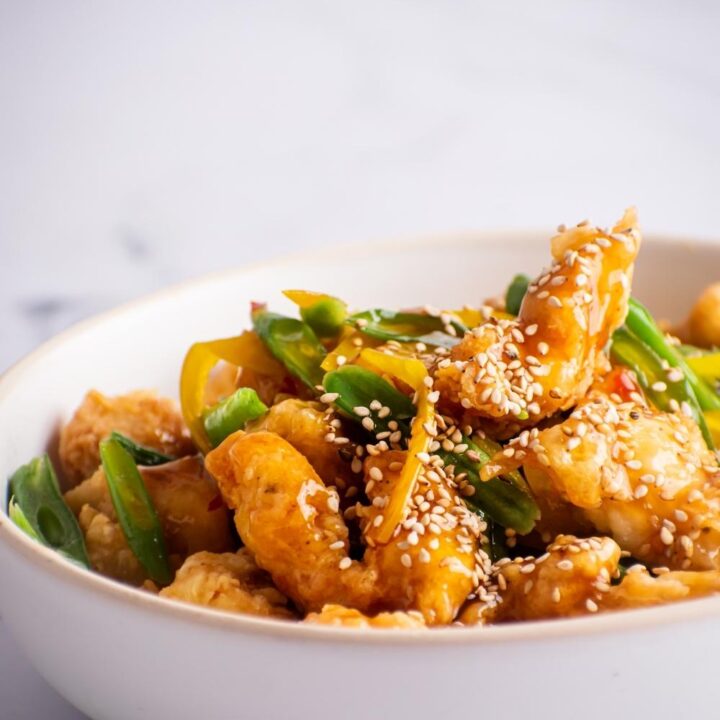 A bunch of pieces of honey sesame chicken in a white bowl.