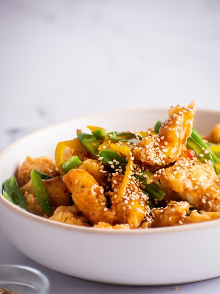 A bunch of pieces of honey sesame chicken in a white bowl.