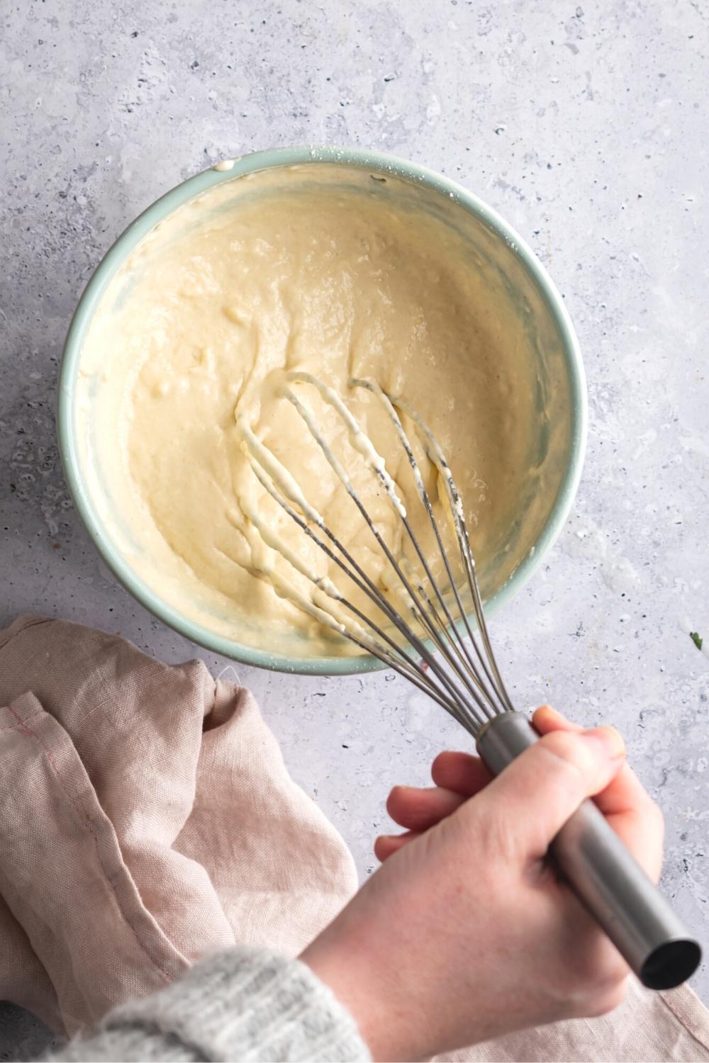 A hand whisking together Denny's pancake ingredients.