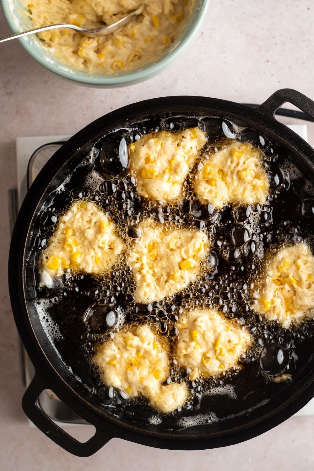 Seven corn nuggets frying in oil in a frying pan.