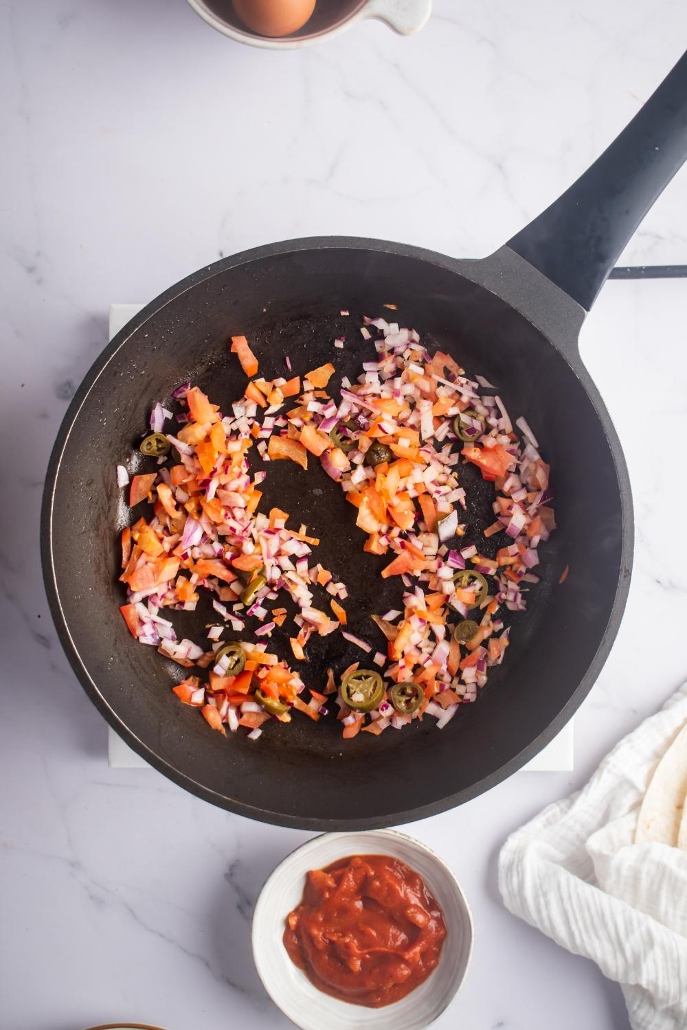 Tomatoes, onion, and jalapeños in a skillet.