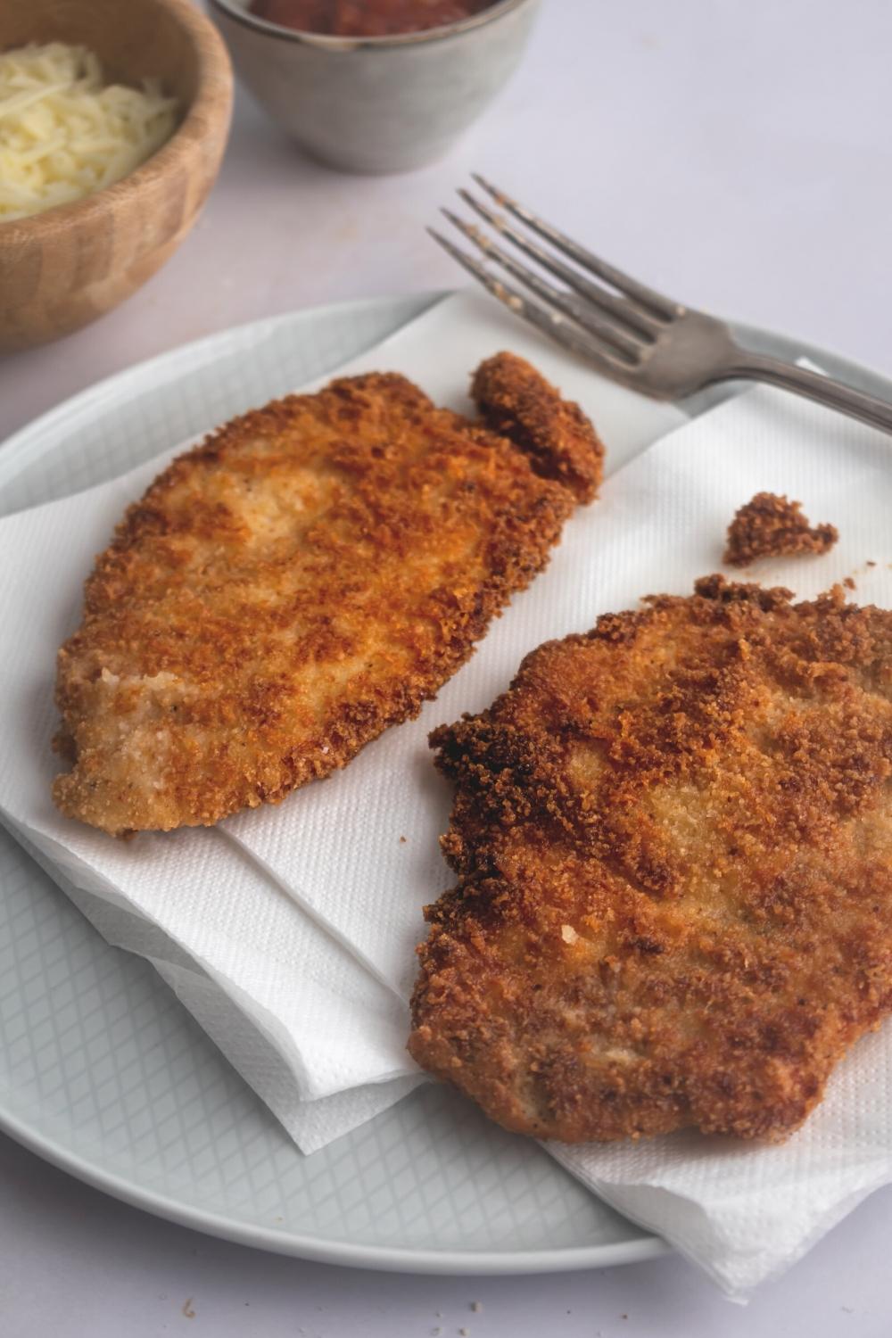 Two pieces of breaded chicken on paper towels on a plate.