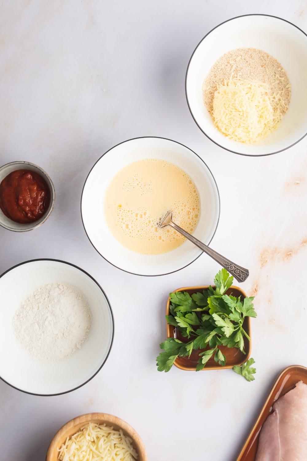 A bowl of flour, a bowl whisk egg, in a bowl of breadcrumbs and she's all of the diagonal line on a white counter