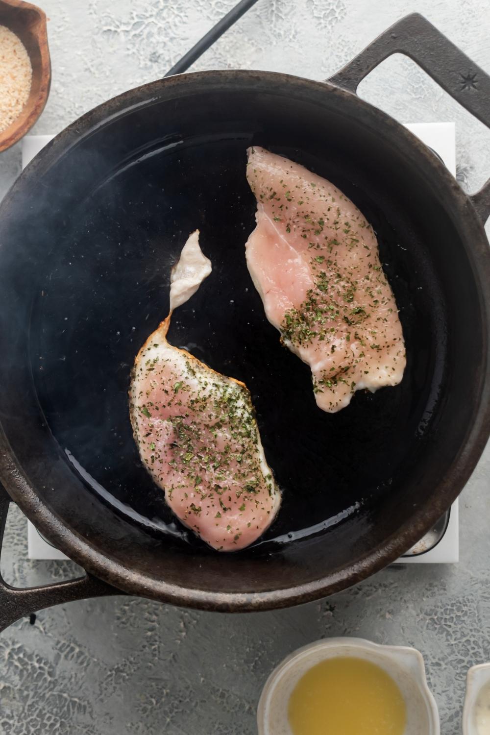 Two pieces of chicken breast in a skillet.