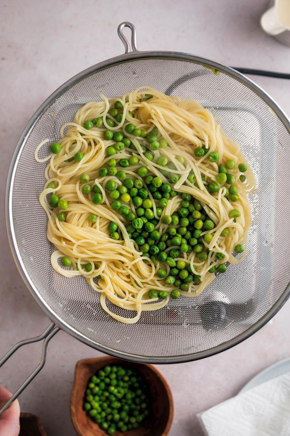 Cooked spaghetti and peas in a strainer.