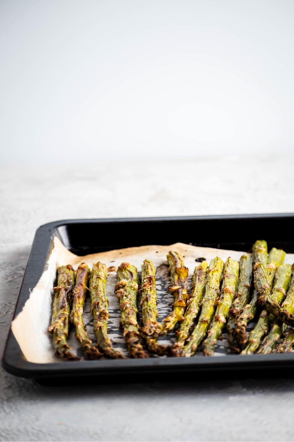 A bunch of asparagus spears on a piece of parchment paper in part of a baking sheet..