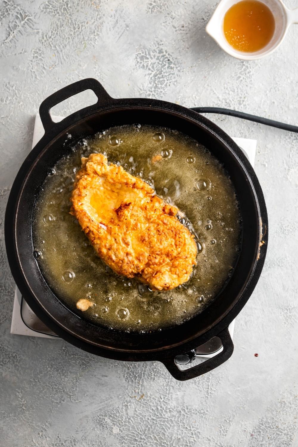 A piece of breaded chicken frying in a pan filled with oil.