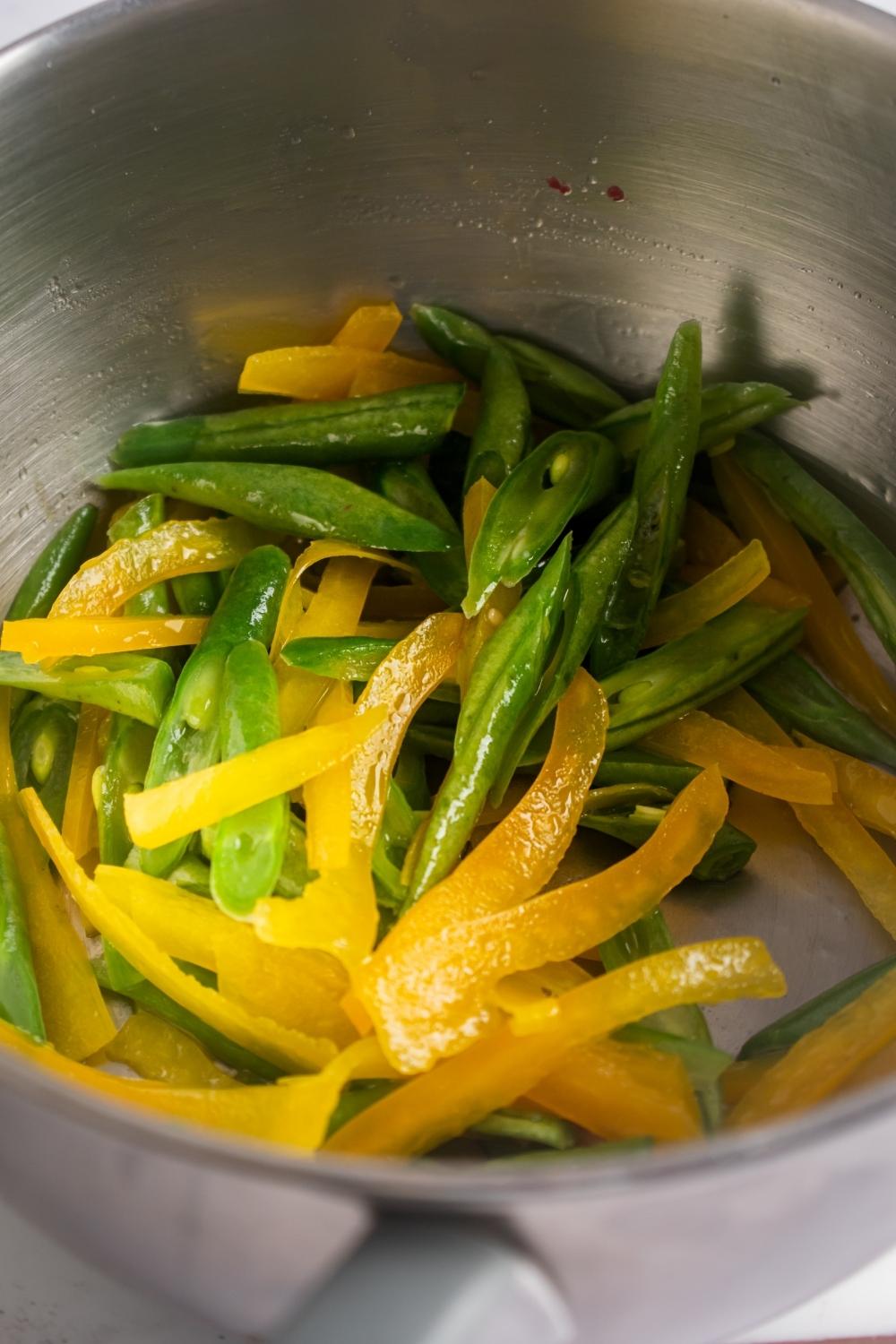 Green beans and sliced yellow red bell peppers in a gray pot.
