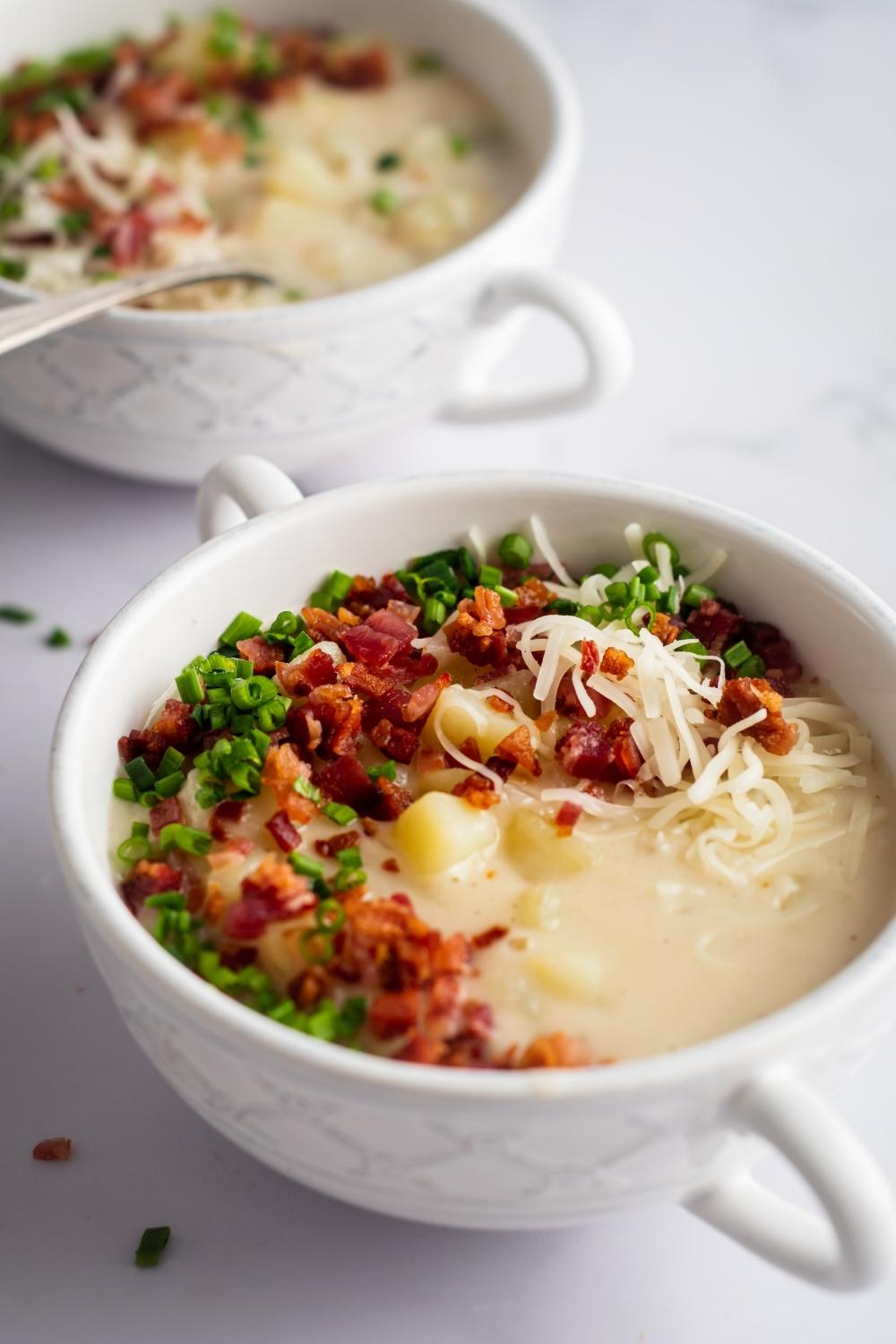 Chives, bacon, shredded cheese, creamy broth, and potatoes in a white bowl.