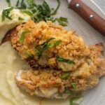 Two pieces of longhorn parmesan crusted chicken and mashed potatoes on a white plate.