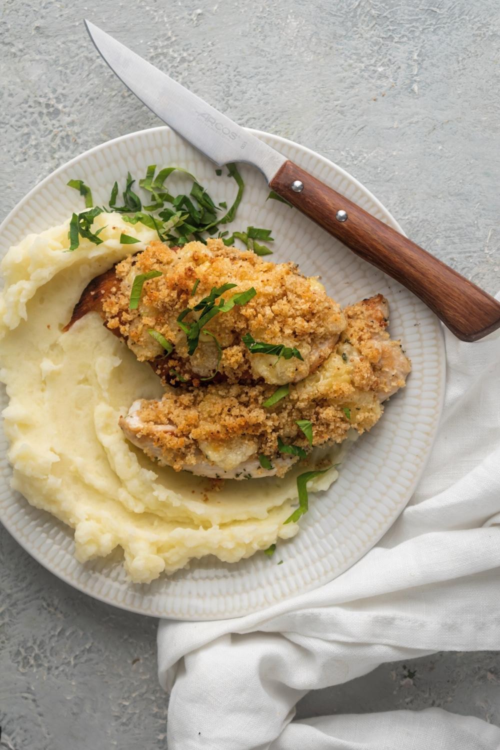 Two parmesan crusted chicken breasts on top of one another next to mashed potatoes all on a white plate.