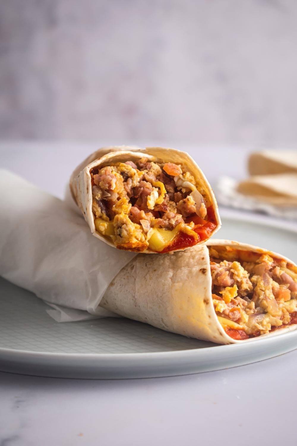 Two breakfast burritos on top of one another on a gray plate on a white counter.