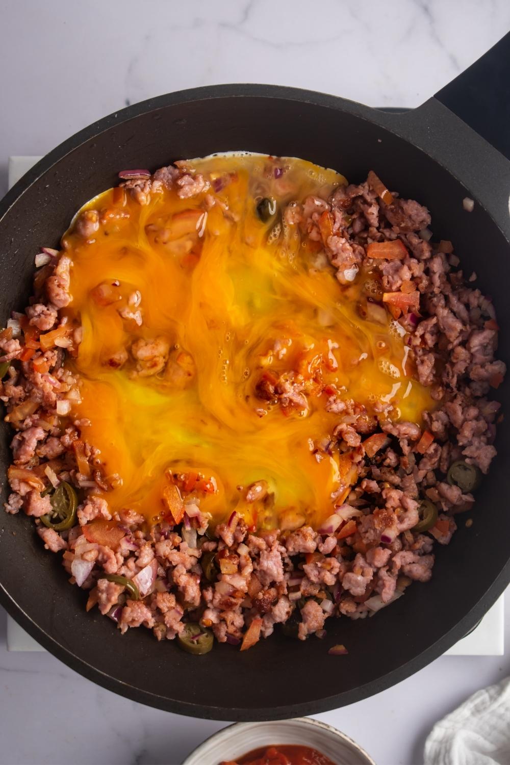 An egg on top of chopped onion, jalapenos, tomatoes, and ground beef in a skillet