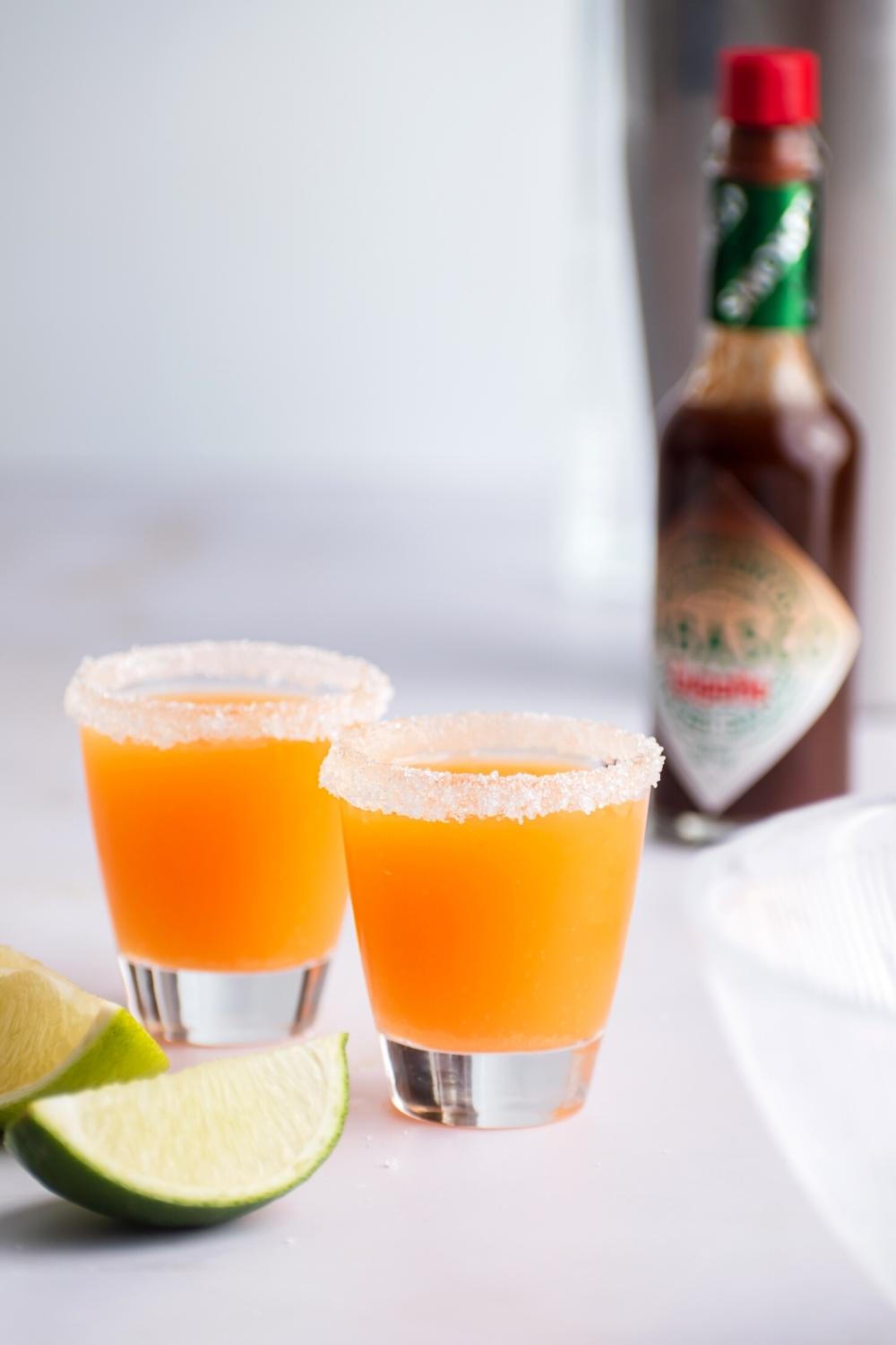 Two mexican lollipo shots on a white table with a bottle of tobasco behind it.