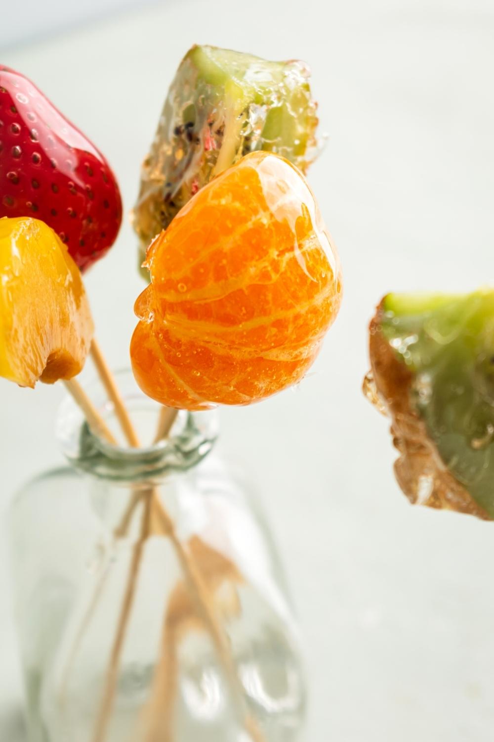 A bunch of pieces of tanghulu on woodedn skewers in a glass vase.