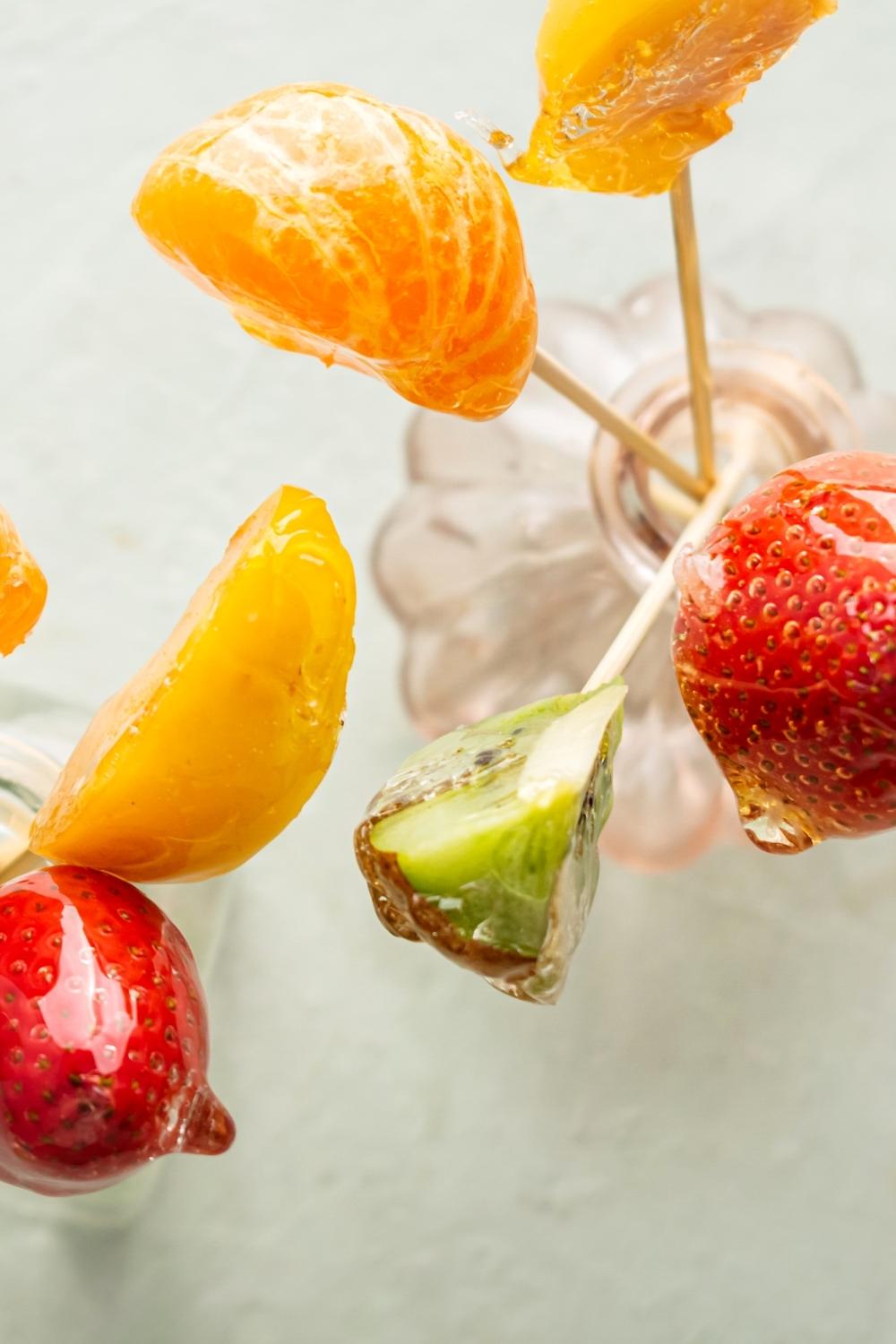 A strawberry, apricot, orange, and Keewee all on wooden sticks in a glass vase.