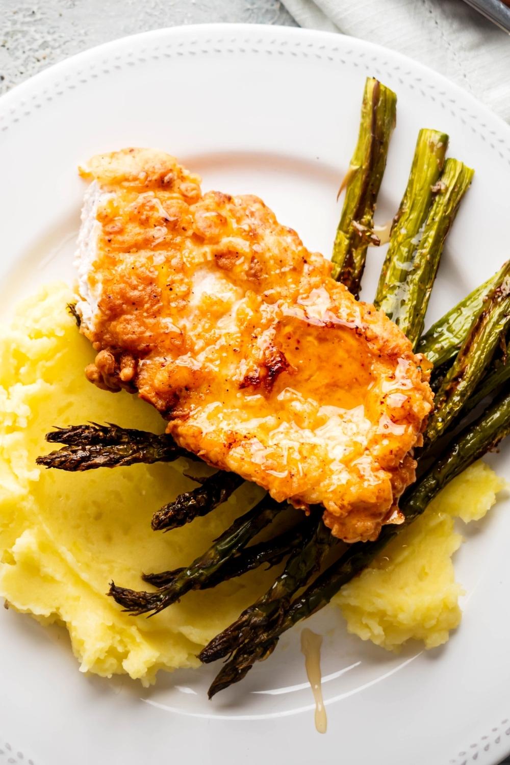 Shuffle honey on top of chicken that is an asparagus spears on top of mashed potatoes on a white plate.