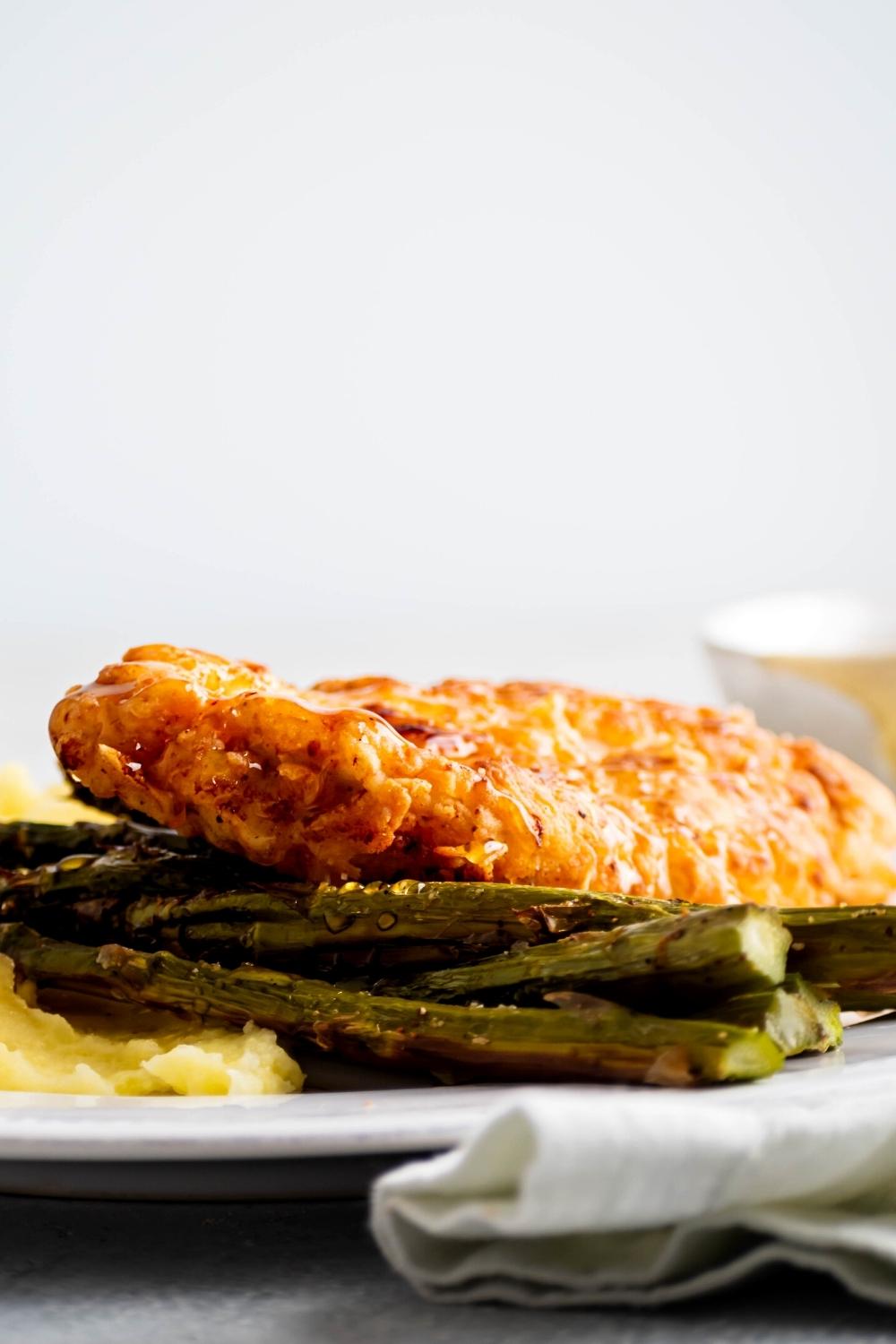 A piece of truffle honey chicken on part of asparagus on part of some mashed potatoes on part of a white plate