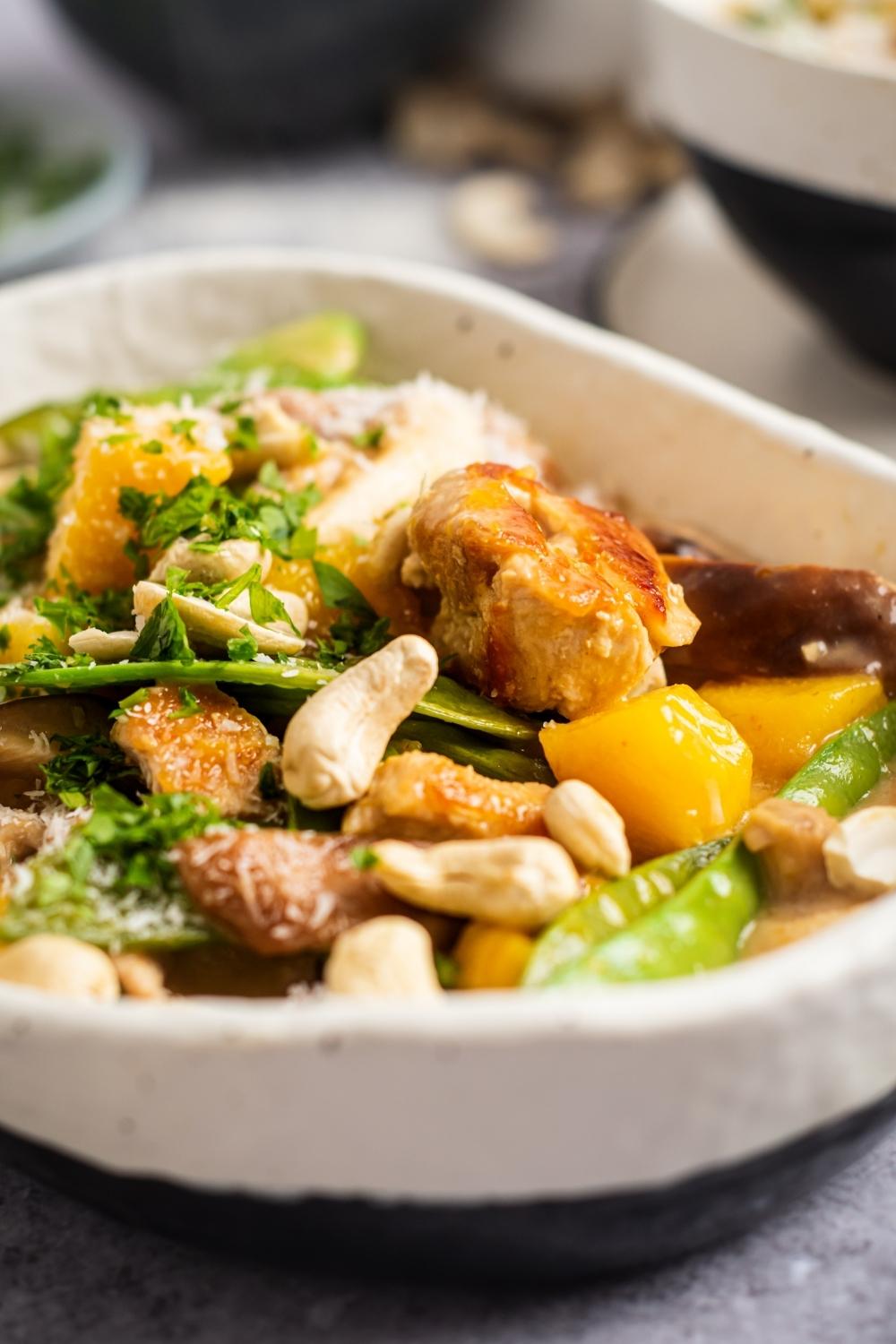 Ceramic bowl with golden browned chicken, cashews, snap peas, and mango mixed together