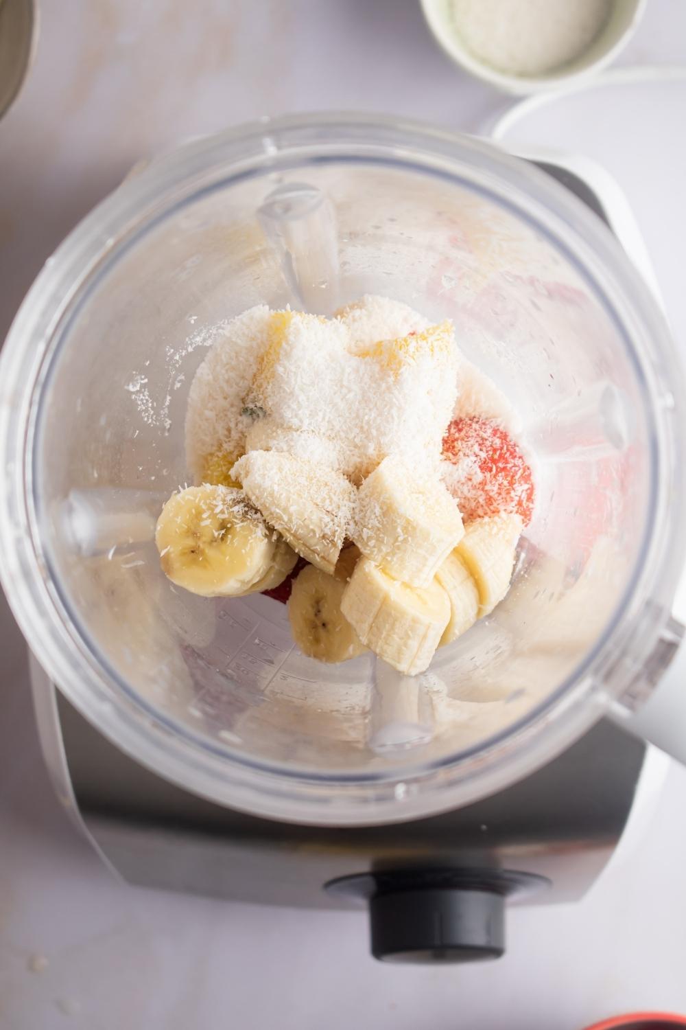 A blender with banana, strawberry, white chocolate, and pineapple in it.