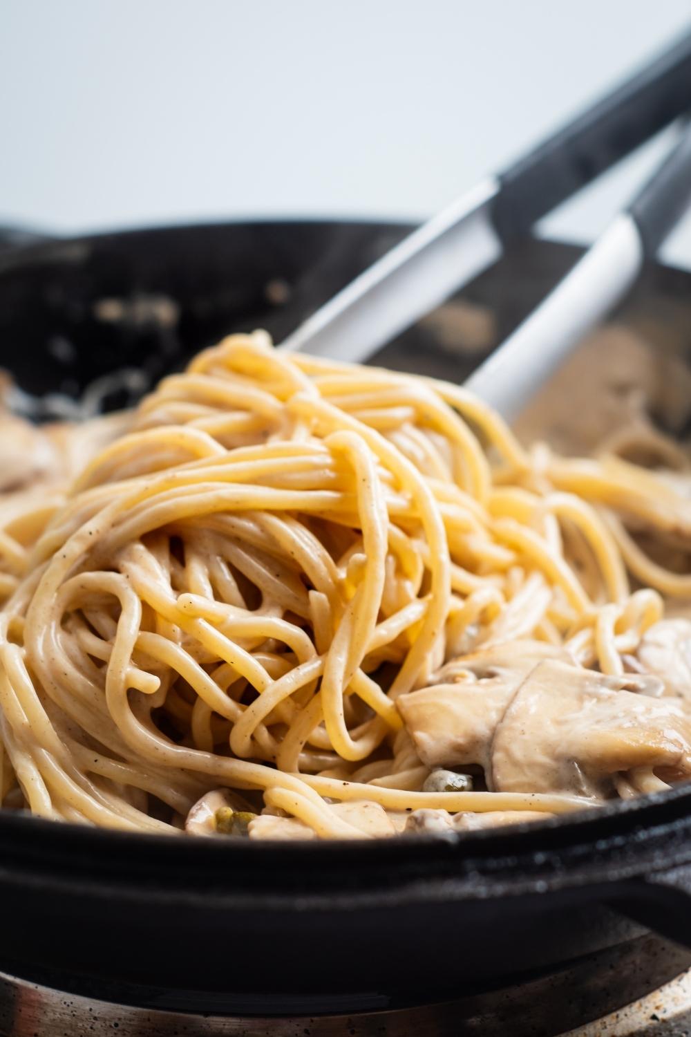 a skillet with cooked spaghetti pasta and creamy sauce with mushrooms.