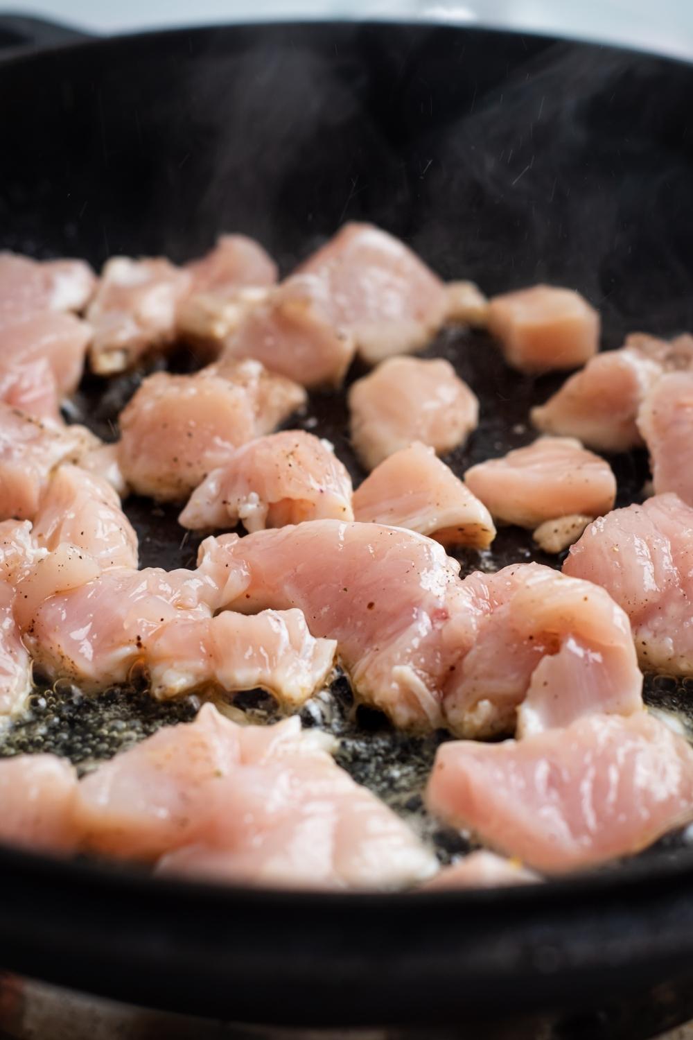 A skillet with uncooked chicken cubes.