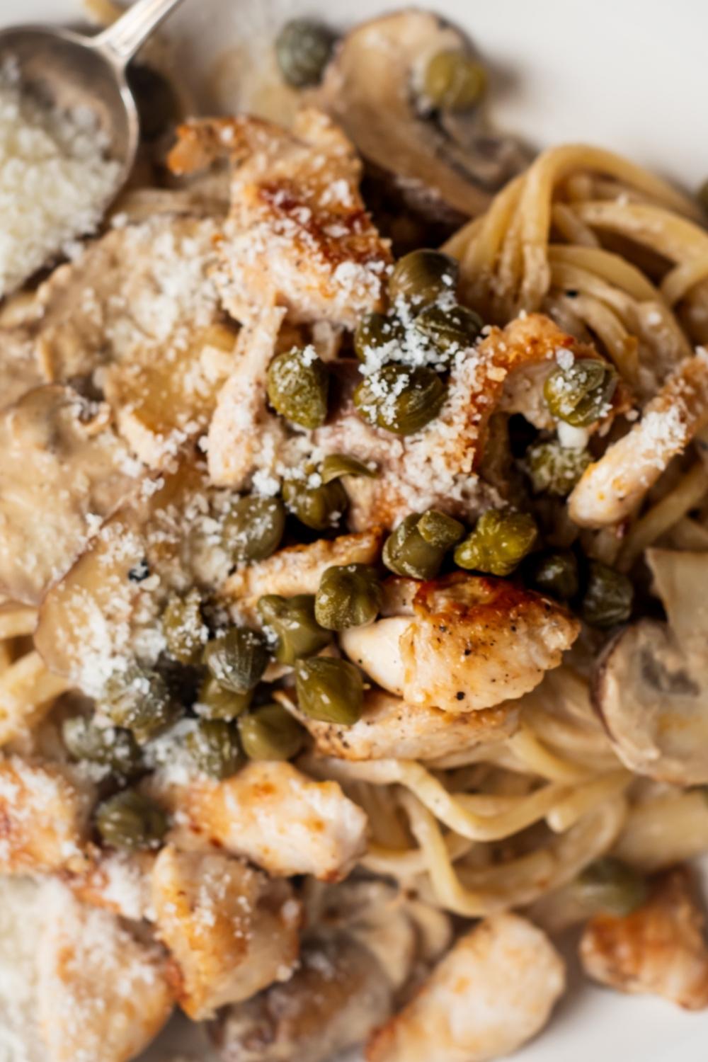 A close up of cheesecake factory chicken piccata topped with capers and parmesan cheese.