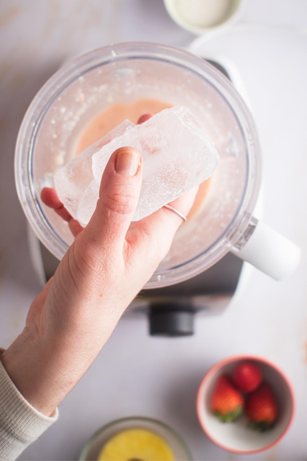 A hand holding ice cubes over a blender with Bahama mama smoothie in it.