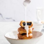 A stack of fried Oreos in a ceramic bowl with blaze being poured from a spoon onto them.