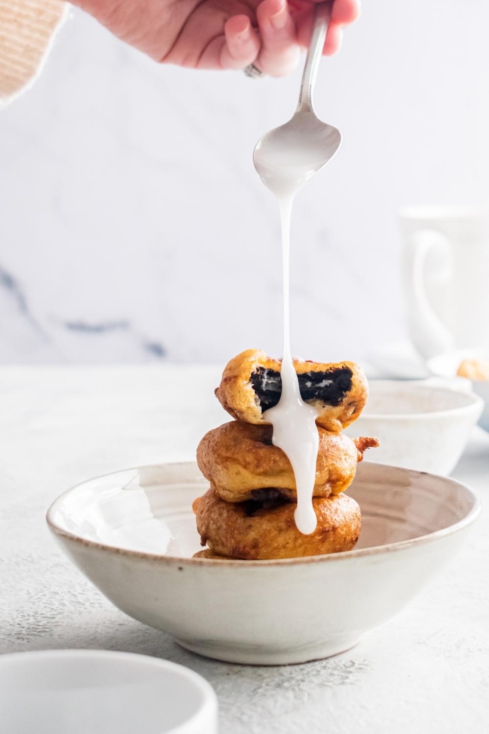 A stack of fried Oreos in a ceramic bowl with blaze being poured from a spoon onto them.