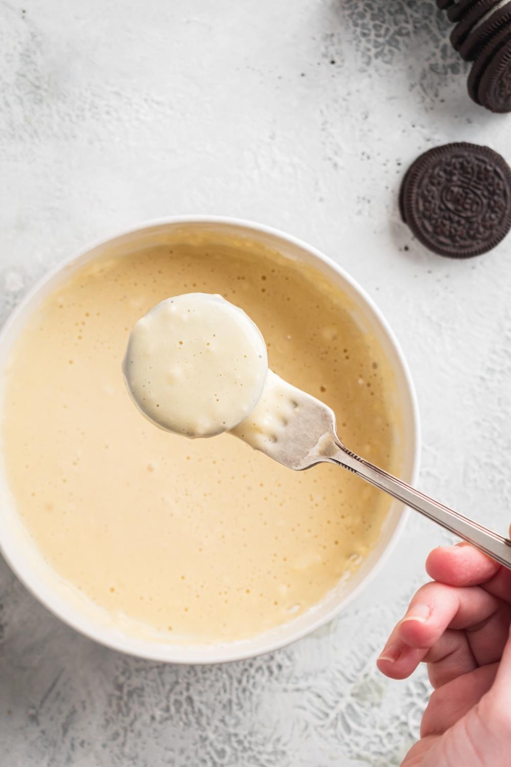 An Oreo covered in pancake batter, over the bowl of batter on a fork.