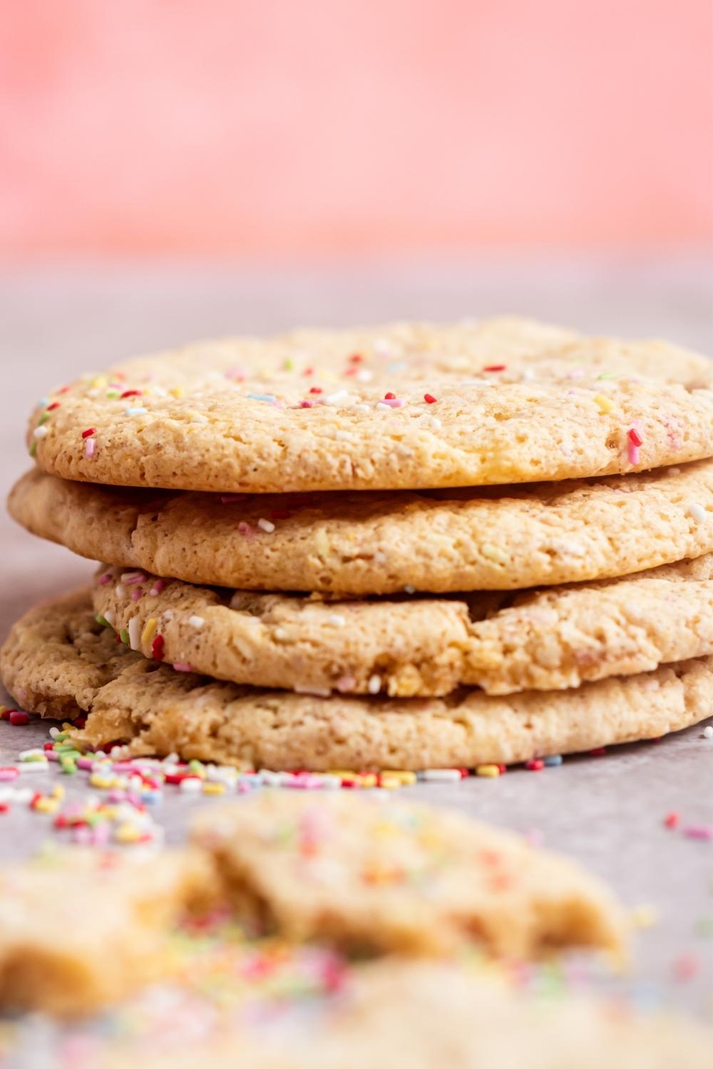 A stack of four funfetti cookies with rainbow sprinkles on top and surrounding the stack.