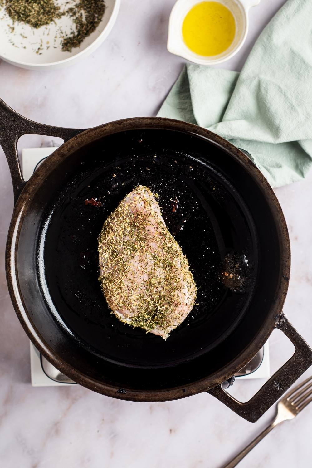 A piece of herb crusted chicken in a skillet.