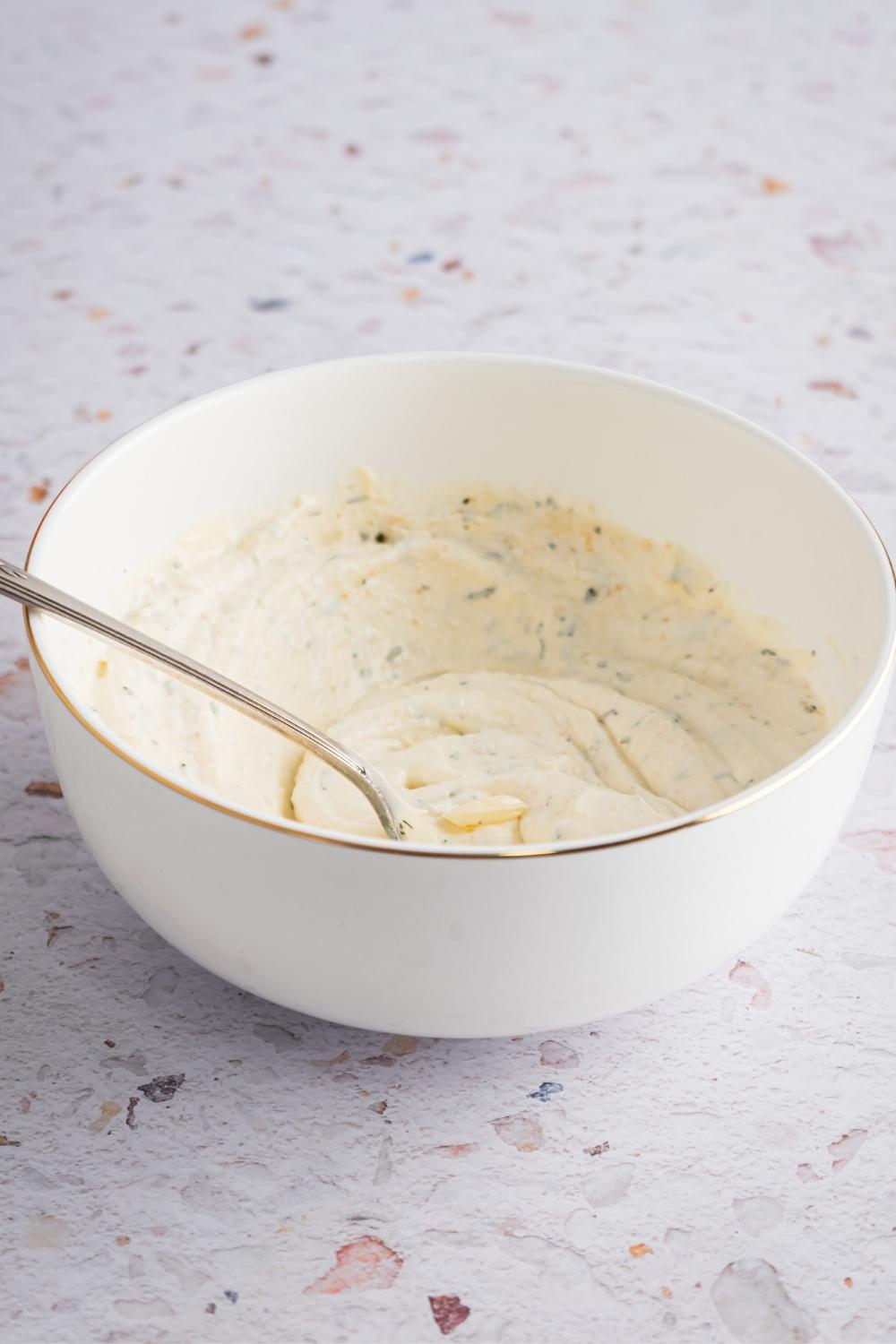 A white bowl with ranch dressing in it.