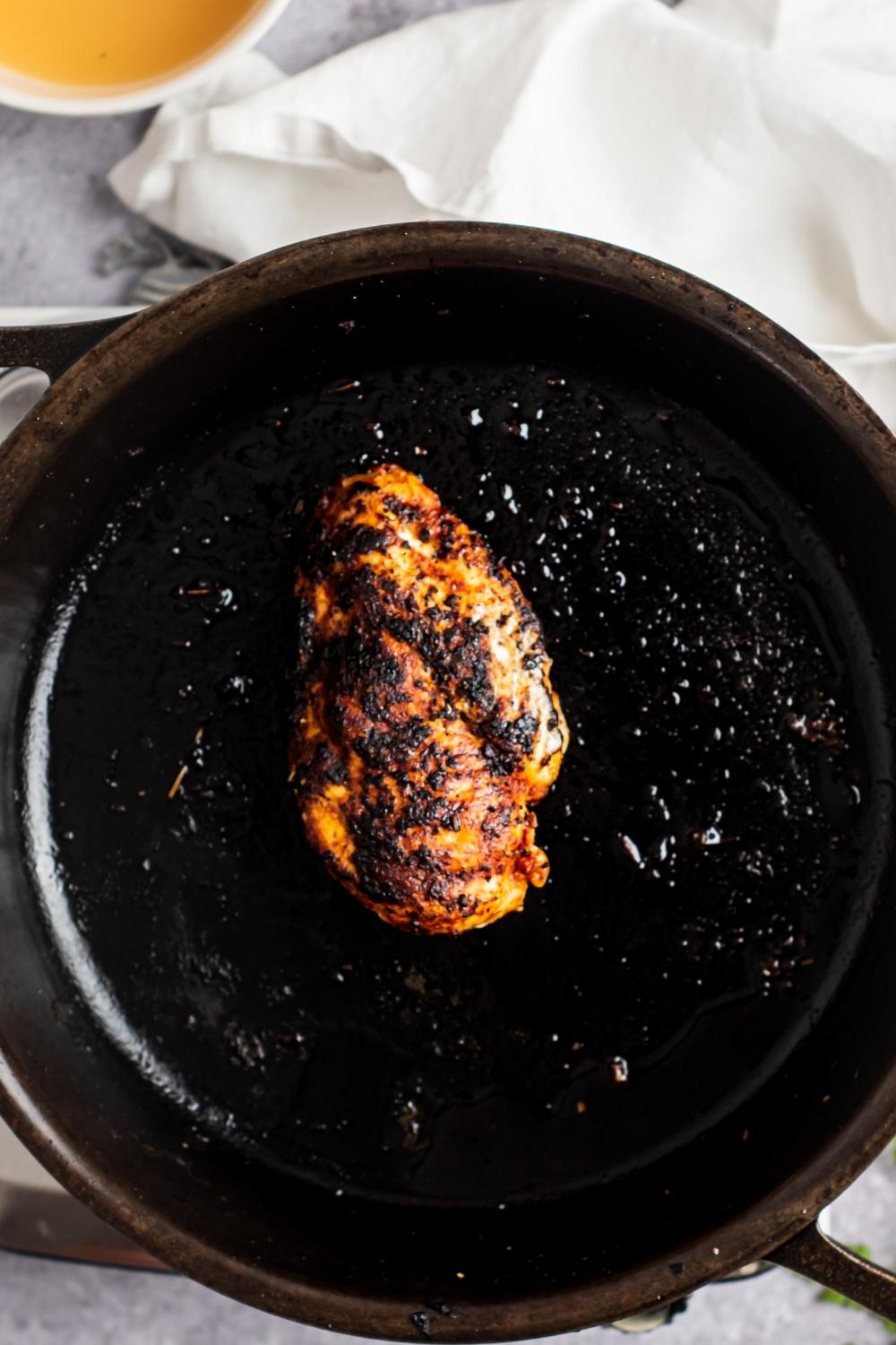 Overhead view of a skillet with a charred chicken breast.