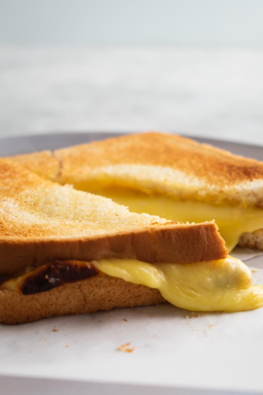 A close-up of an air fryer grilled cheese sandwich sliced in half with melted cheese overflowing the slices.