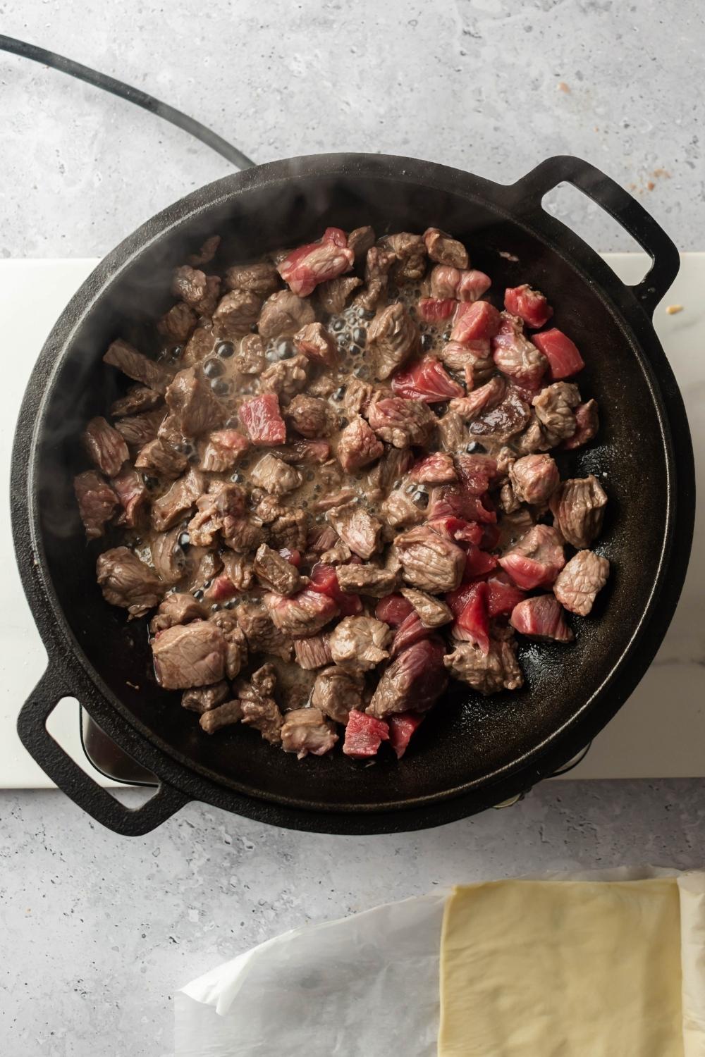 An overhead view of beef chunks being cooked in an iron pot.